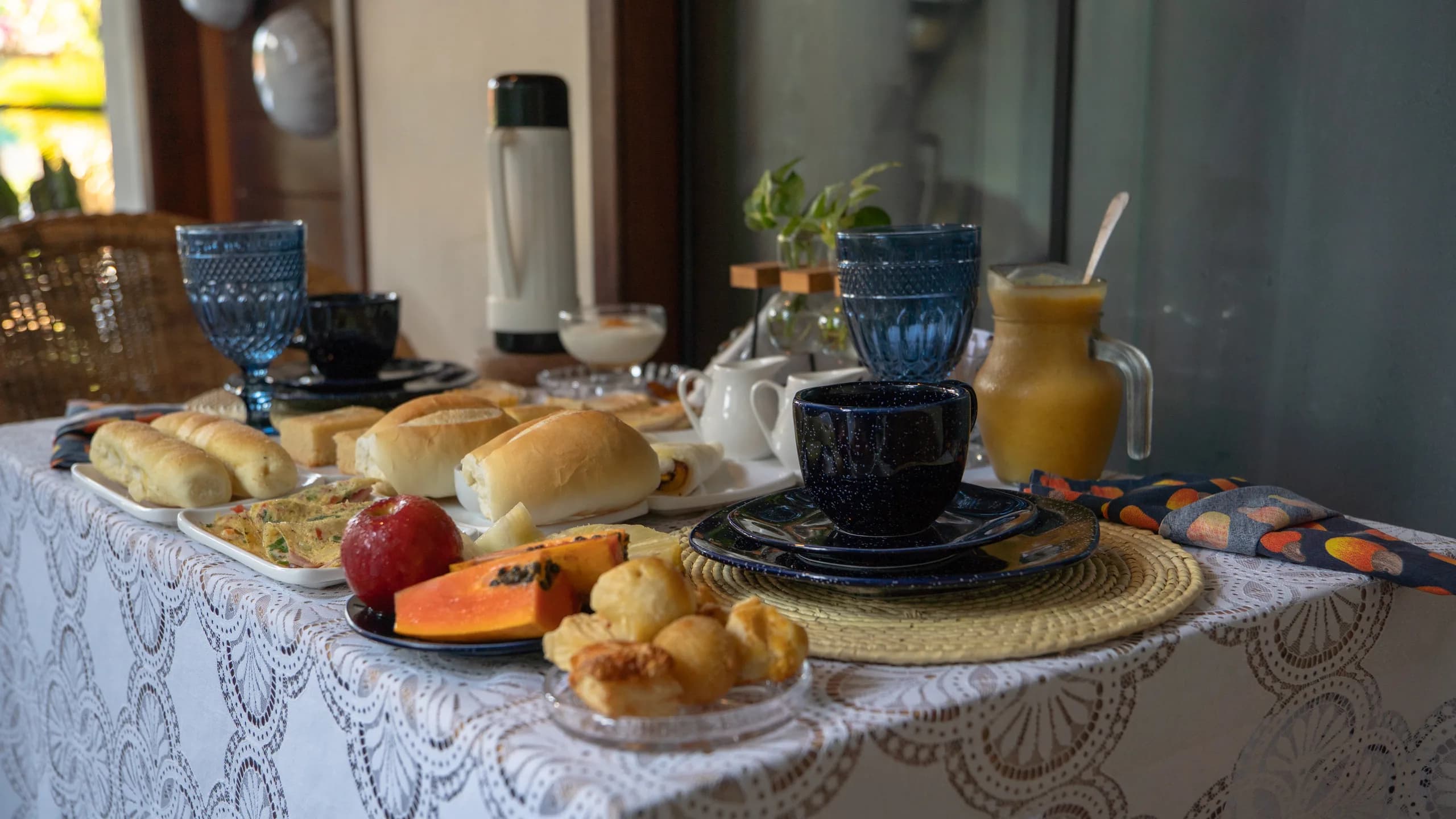 Detalhe da mesa de café da manhã com pães, omelete, frutas frescas e suco